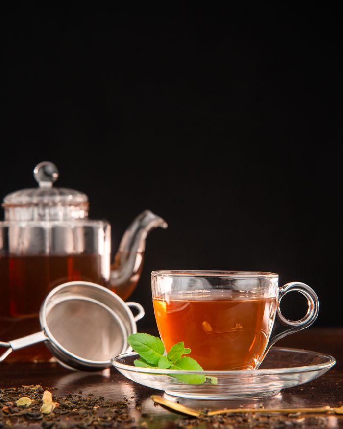 Glass teacup with fresh tea, herbs, and infuser; elegant and inviting.