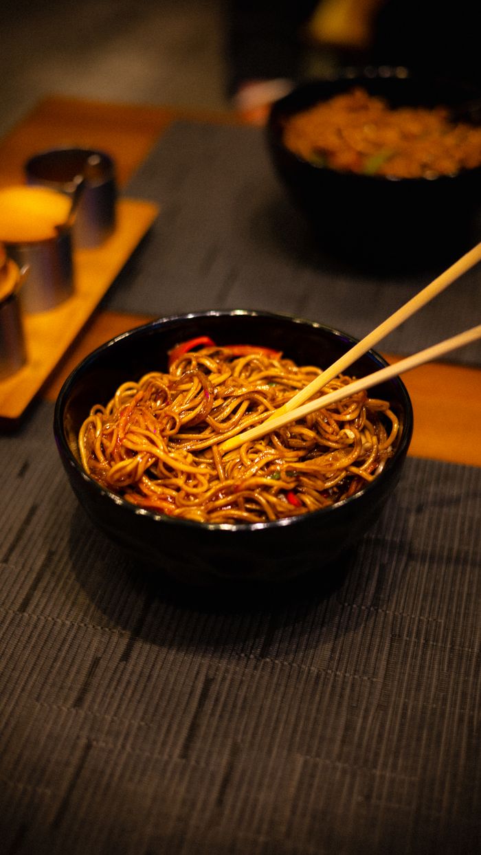 A close-up of tasty noodles in a black bowl with chopsticks on a table ready to eat.