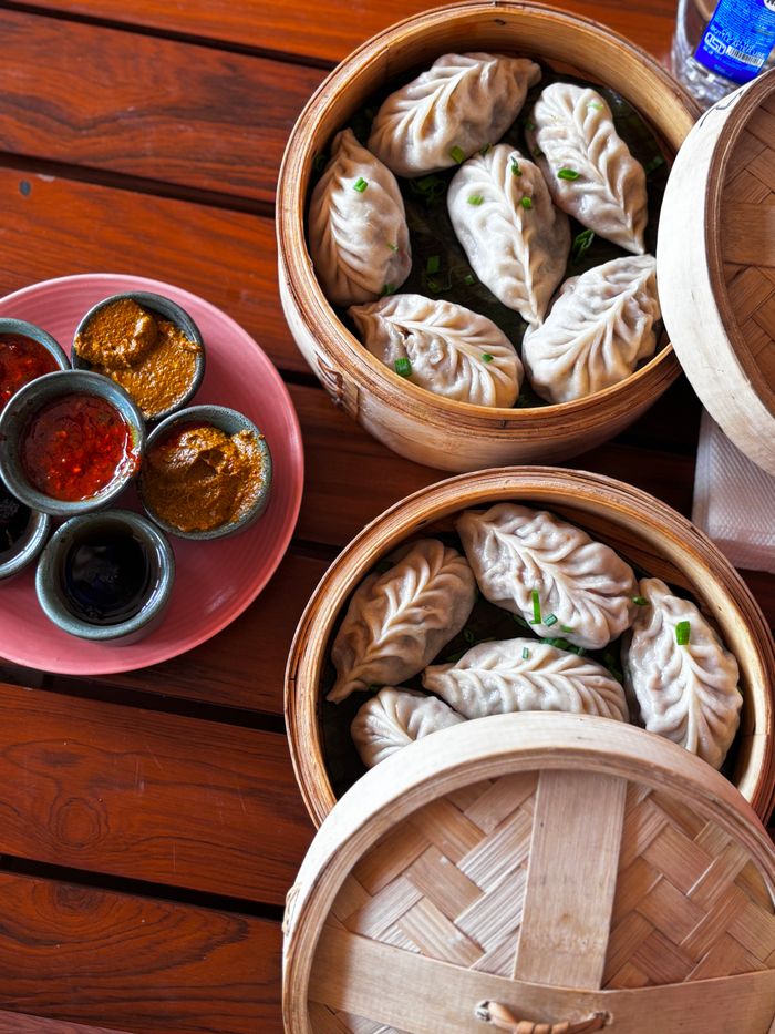Top view of steamed dumplings in bamboo baskets with various Asian dipping sauces on a rustic table.