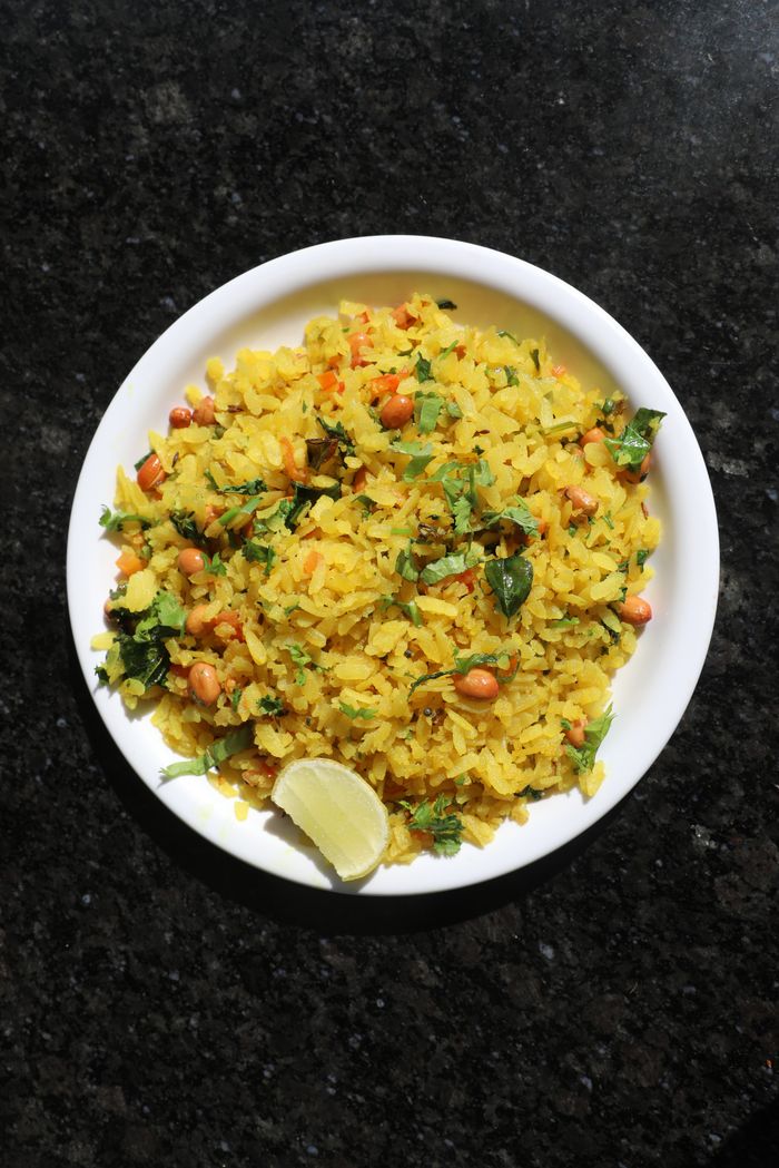 Delicious and vibrant Indian poha served with a lime wedge on a white plate.