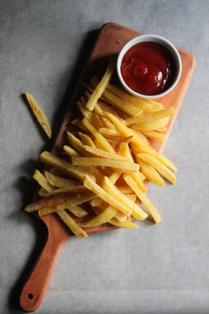 Golden french fries served with ketchup on a rustic wooden board.